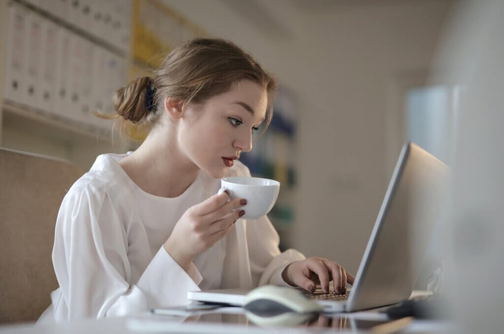 A lady seated with a laptop and holding a cup - Summer Design Internship at OutWitly