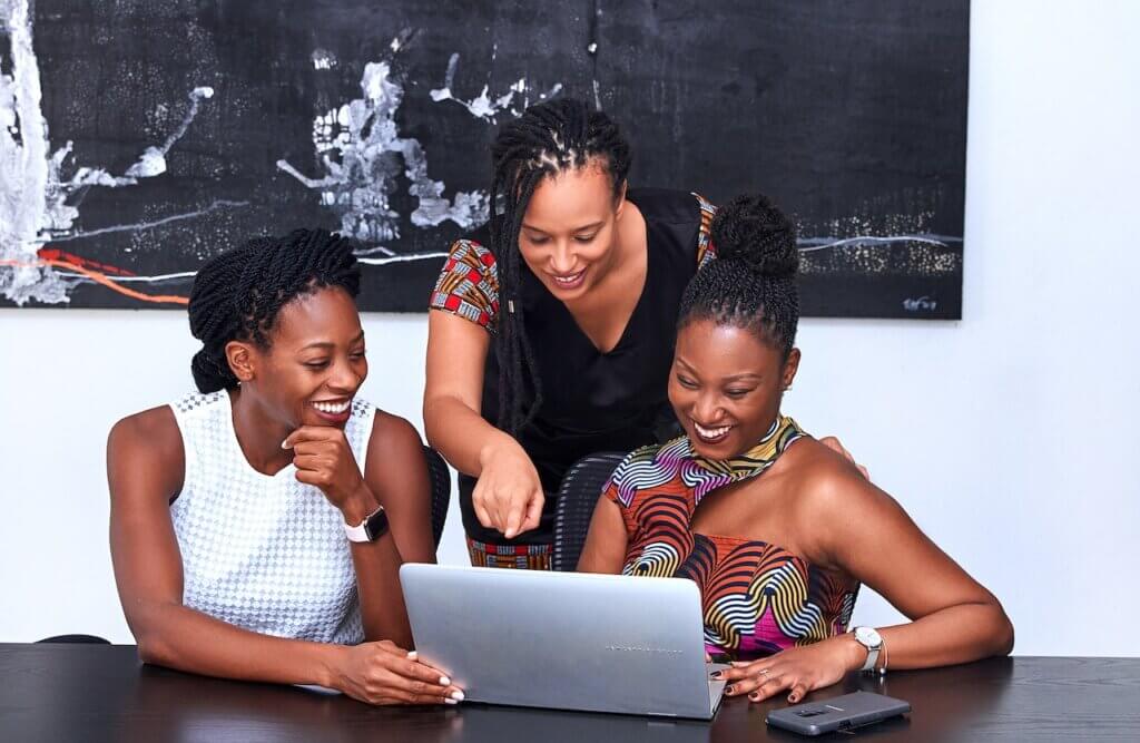 Three women looking at a desktop on a desk - PWC is hiring a User Experience Designer