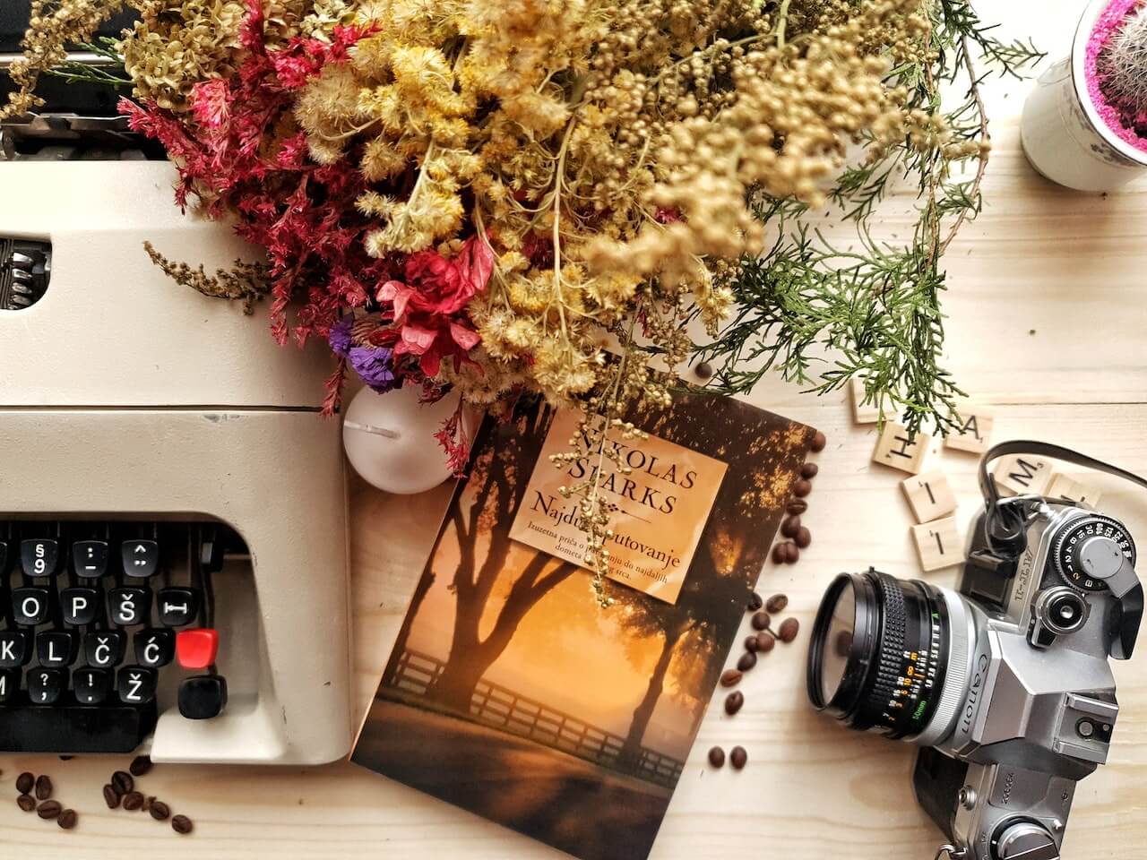 A picture of a type writer, a novel and a camera on a table adorned with flowers