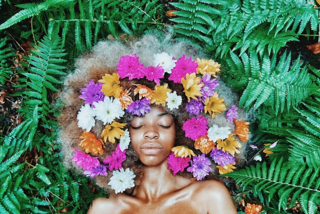 A lady lying on a grass with a flower brand on her afro hair